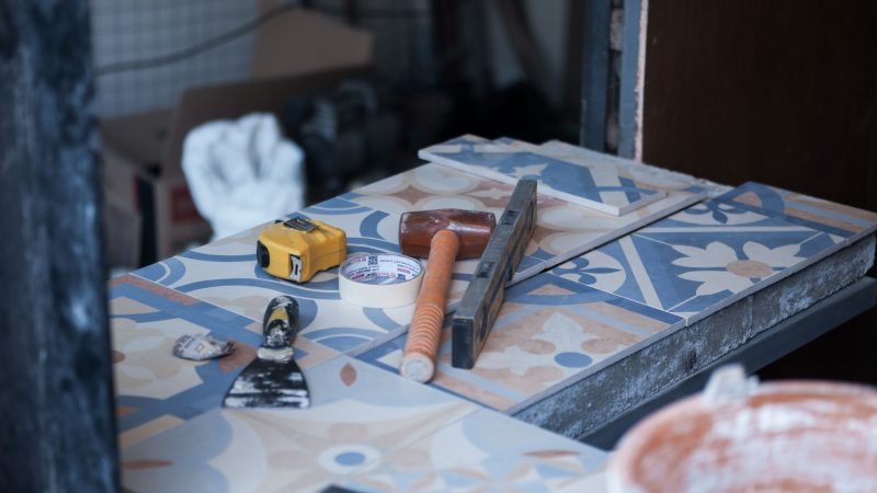Tools and tiles on a construction site, ready for tiling work. Includes trowel, tape measure, and adhesive tape.